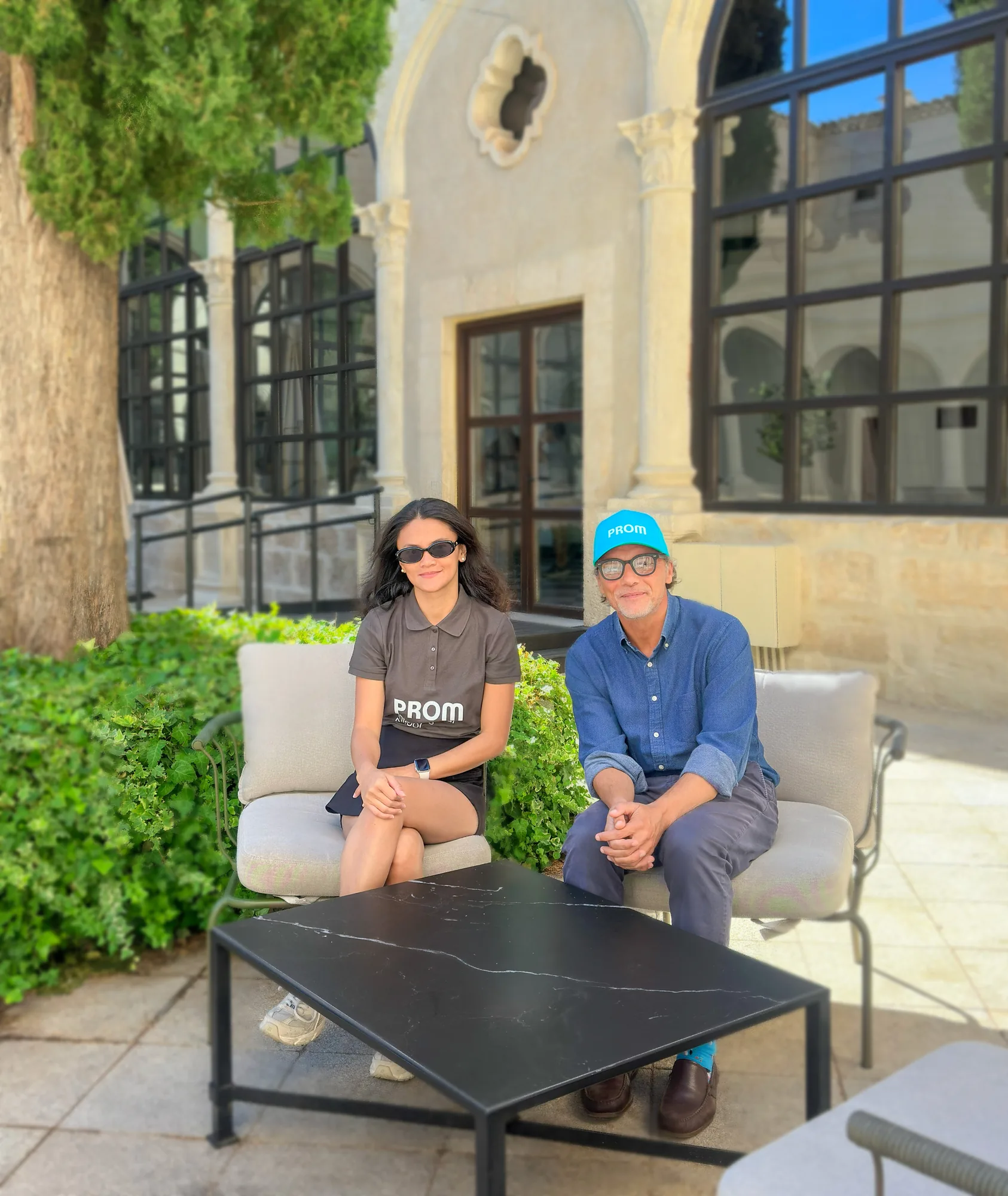 Dos personas conversando sentadas en un patio con vegetación